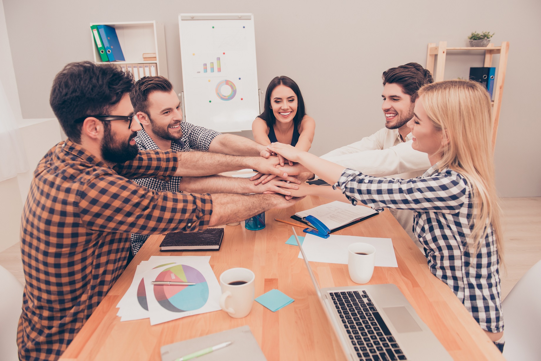 young business team putting their hands on top of each other at conference and smiling